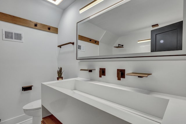 bathroom featuring hardwood / wood-style floors, vanity, lofted ceiling, and toilet