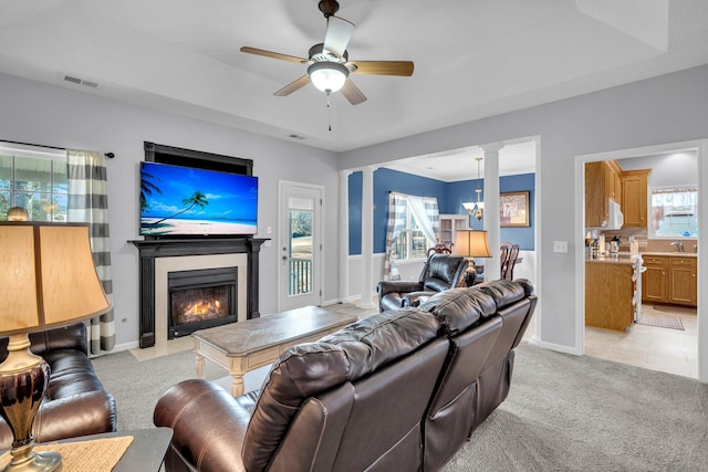 carpeted living room featuring decorative columns, ceiling fan with notable chandelier, a tray ceiling, and sink