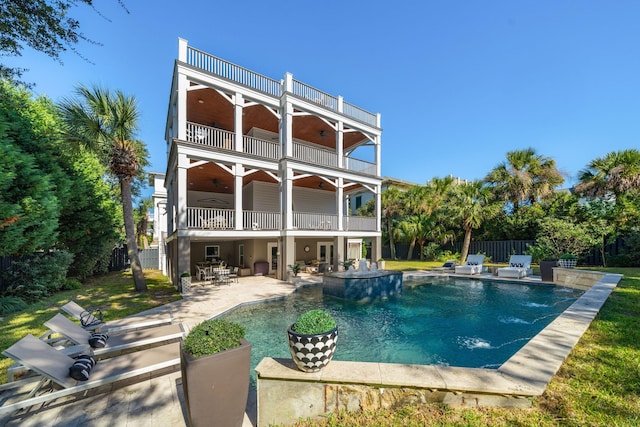 rear view of property featuring a balcony, a yard, a patio, and a fenced in pool