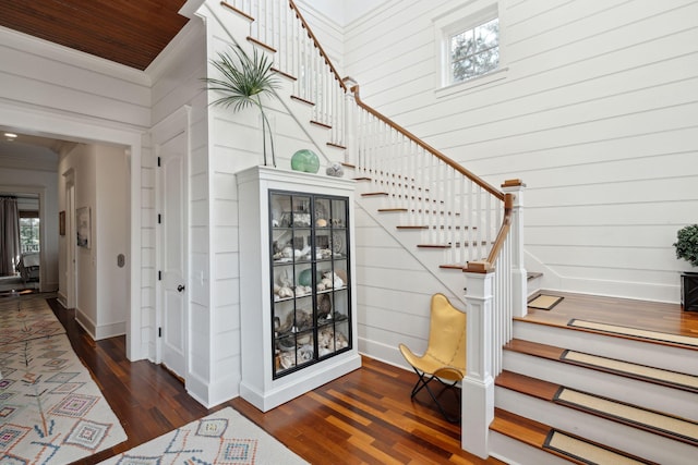 stairway with hardwood / wood-style flooring, wooden walls, a towering ceiling, and crown molding