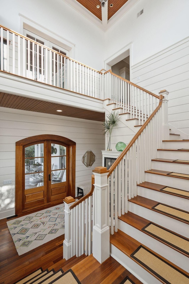 interior space with wood walls, ornamental molding, french doors, dark wood-type flooring, and a towering ceiling