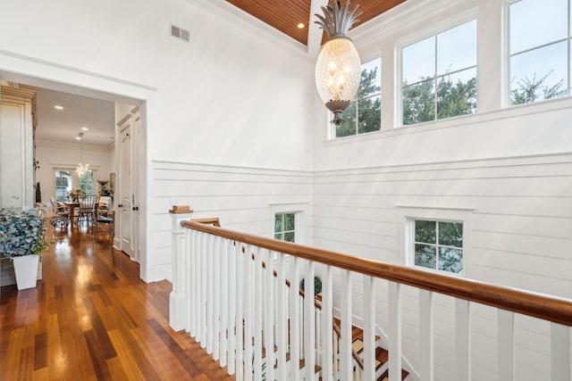 corridor featuring a notable chandelier, ornamental molding, a towering ceiling, and dark wood-type flooring