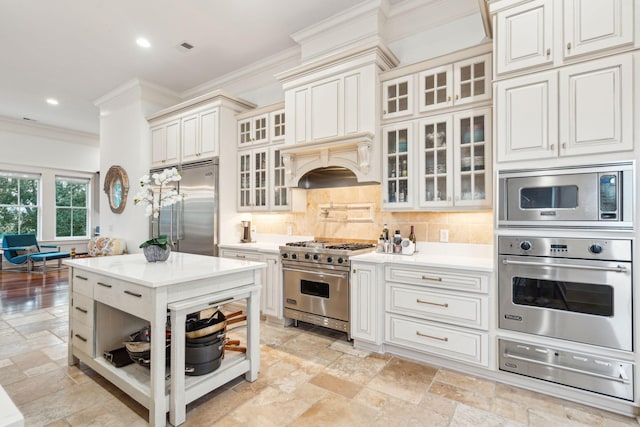 kitchen featuring backsplash, built in appliances, crown molding, and white cabinets