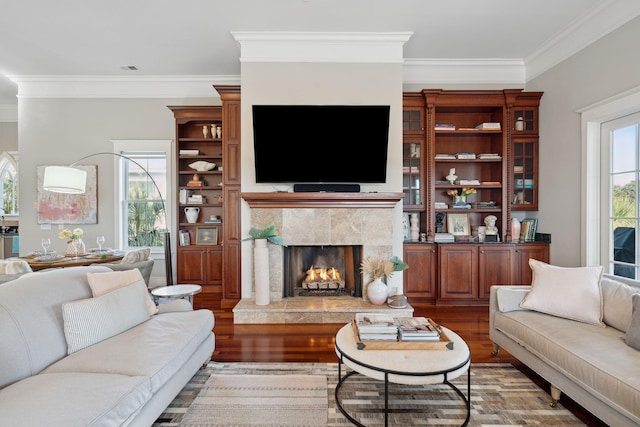 living room featuring wood-type flooring, a premium fireplace, crown molding, and a healthy amount of sunlight