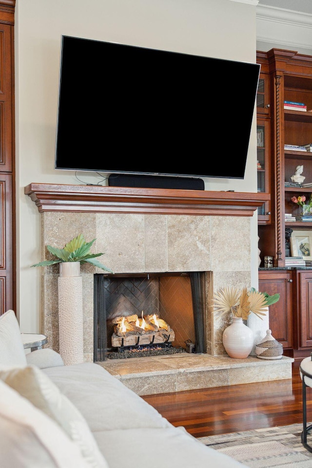 details with wood-type flooring, a tiled fireplace, and ornamental molding