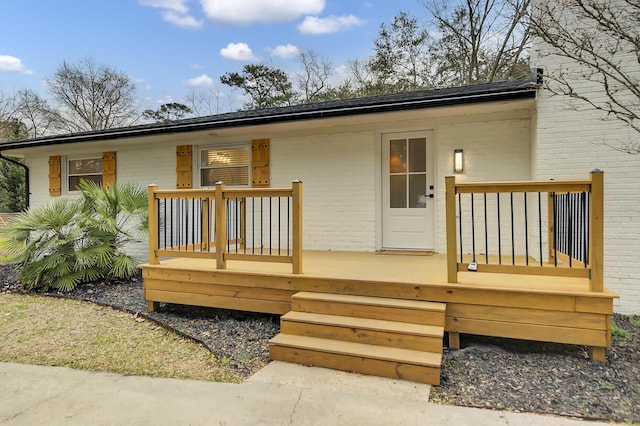 rear view of property with a deck, brick siding, and a shingled roof