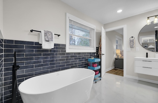 bathroom with vanity, a wainscoted wall, a freestanding tub, recessed lighting, and tile walls