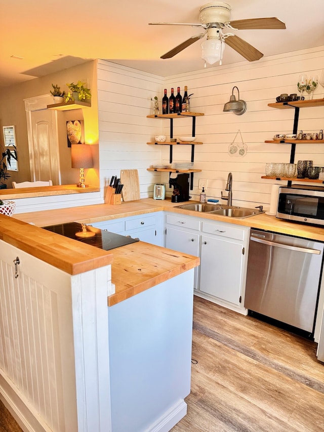 kitchen featuring open shelves, butcher block counters, light wood-type flooring, stainless steel appliances, and a sink