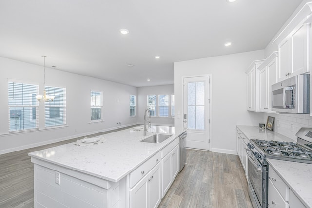 kitchen with white cabinets, a kitchen island with sink, stainless steel appliances, light stone counters, and sink