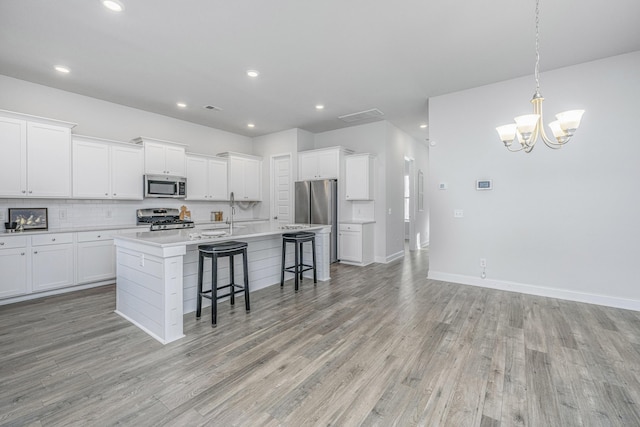 kitchen featuring stainless steel appliances, white cabinetry, a kitchen island with sink, and a breakfast bar area