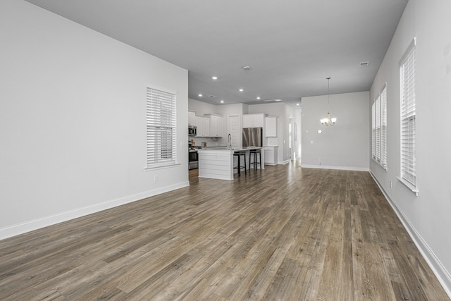 unfurnished living room featuring a notable chandelier, wood-type flooring, and sink