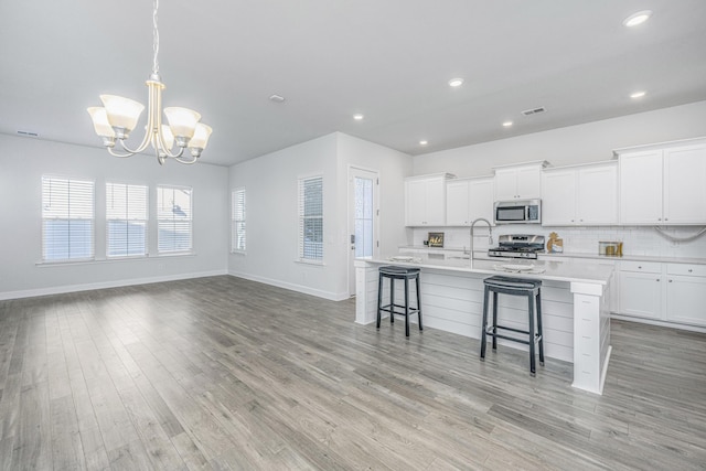 kitchen with stainless steel appliances, white cabinets, a kitchen bar, and a kitchen island with sink