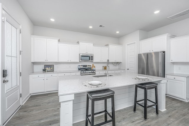 kitchen with sink, stainless steel appliances, an island with sink, and white cabinets