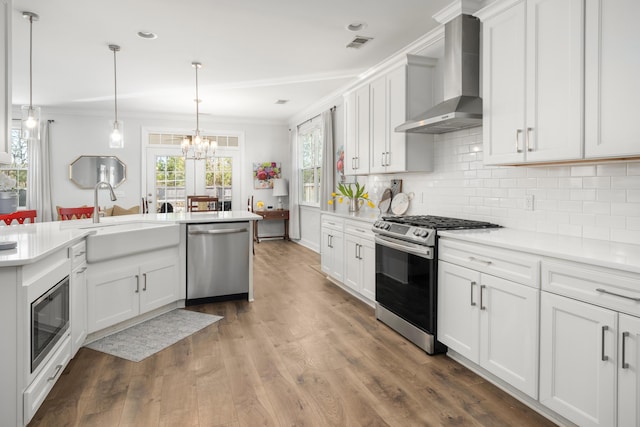 kitchen with wall chimney range hood, light countertops, ornamental molding, appliances with stainless steel finishes, and a sink