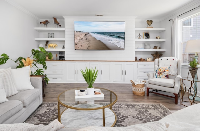 living room with wood finished floors, visible vents, built in shelves, and ornamental molding