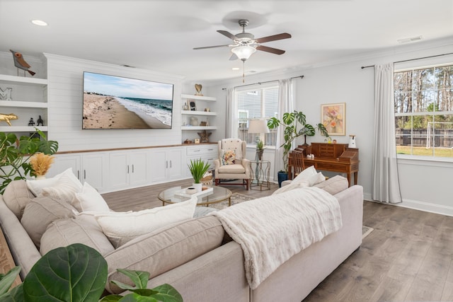 living area with baseboards, crown molding, a ceiling fan, and wood finished floors