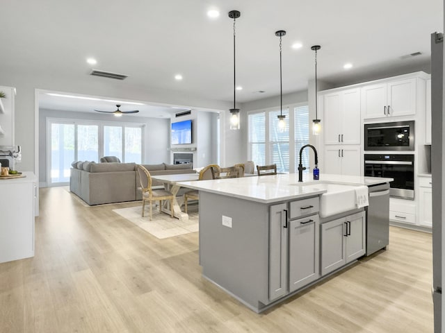 kitchen featuring pendant lighting, sink, appliances with stainless steel finishes, a center island with sink, and light wood-type flooring