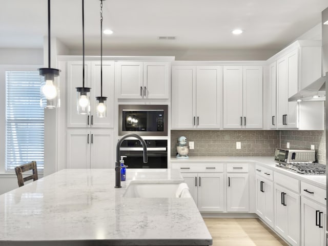 kitchen with white cabinetry, sink, hanging light fixtures, black appliances, and light stone countertops