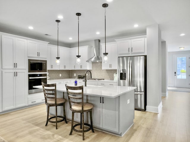 kitchen with white cabinets, decorative light fixtures, stainless steel appliances, and wall chimney exhaust hood