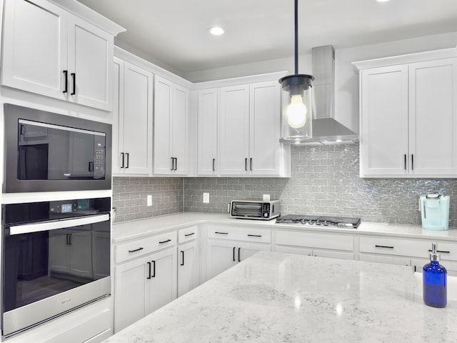 kitchen with tasteful backsplash, hanging light fixtures, wall chimney range hood, stainless steel appliances, and white cabinets