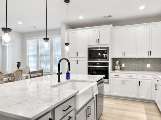 kitchen featuring sink, white cabinetry, decorative light fixtures, an island with sink, and black appliances