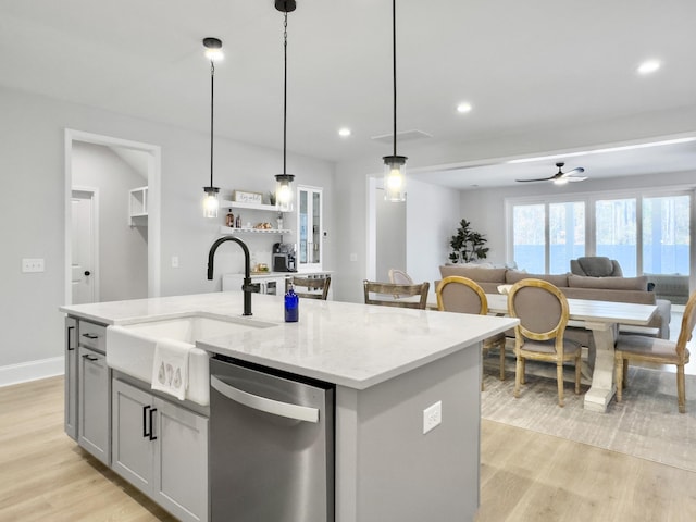 kitchen featuring an island with sink, stainless steel dishwasher, light stone counters, and decorative light fixtures