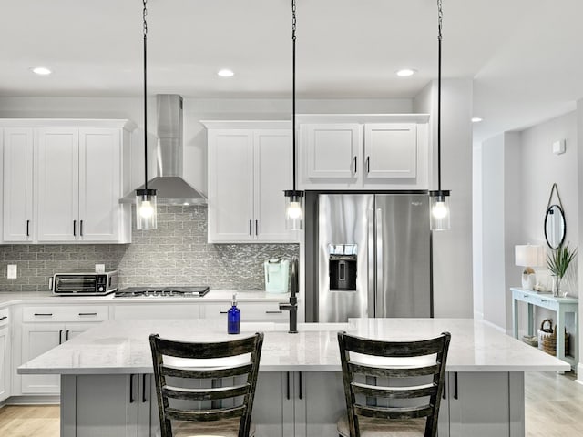 kitchen with wall chimney exhaust hood, light stone counters, appliances with stainless steel finishes, a kitchen breakfast bar, and a kitchen island