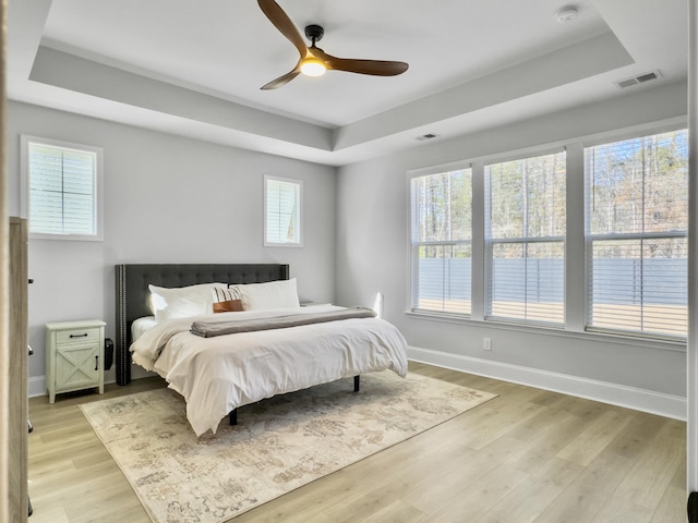 bedroom with light hardwood / wood-style floors, a raised ceiling, and ceiling fan