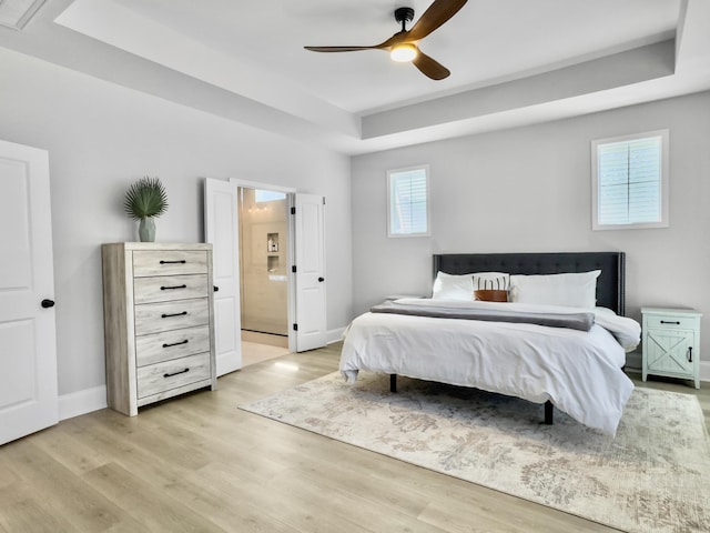 bedroom featuring ceiling fan, light wood-type flooring, and a tray ceiling