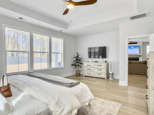 bedroom featuring multiple windows, ceiling fan, a raised ceiling, and light hardwood / wood-style floors