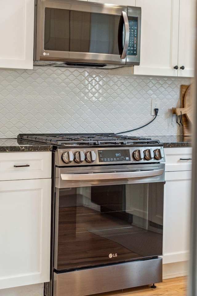 kitchen with white cabinets, stainless steel appliances, and dark stone countertops