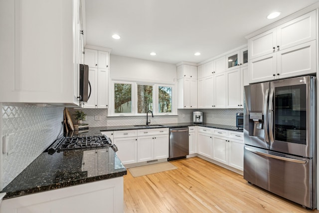 kitchen with sink, black appliances, dark stone countertops, white cabinets, and light hardwood / wood-style floors