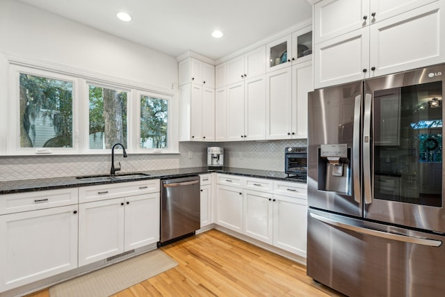 kitchen with sink, dark stone countertops, light hardwood / wood-style floors, white cabinetry, and stainless steel appliances