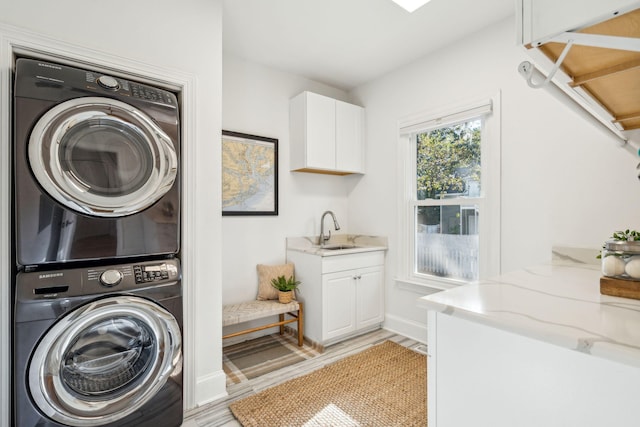 clothes washing area featuring light wood-type flooring, stacked washer / drying machine, and sink