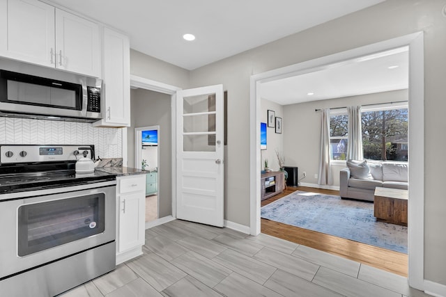 kitchen featuring backsplash, baseboards, open floor plan, appliances with stainless steel finishes, and white cabinets