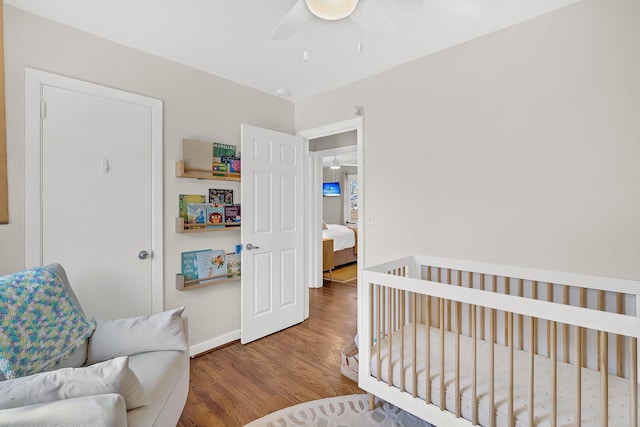 bedroom with a nursery area, wood finished floors, baseboards, and ceiling fan