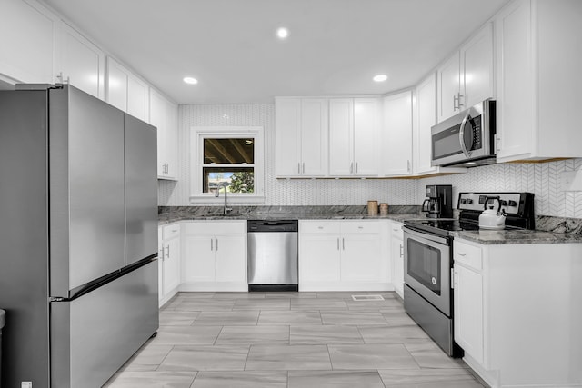 kitchen featuring dark stone countertops, a sink, backsplash, appliances with stainless steel finishes, and white cabinets