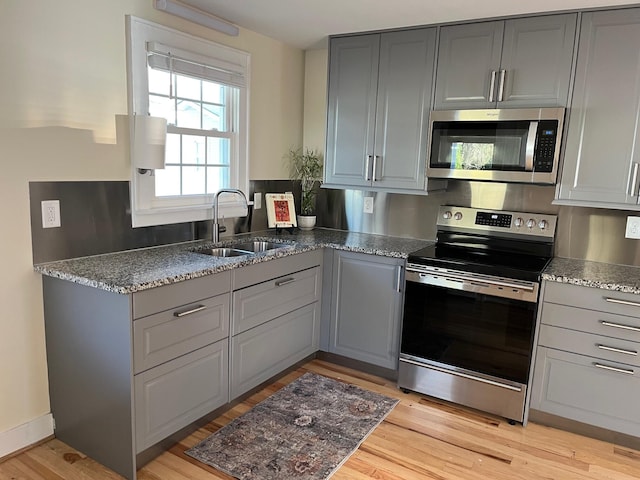 kitchen with stainless steel appliances, gray cabinetry, light wood-style floors, a sink, and dark stone counters