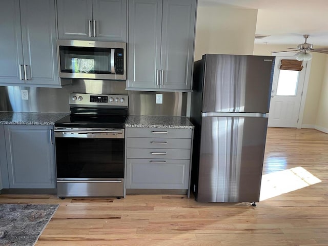 kitchen featuring ceiling fan, light wood-style flooring, appliances with stainless steel finishes, dark stone countertops, and gray cabinets