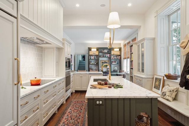 kitchen with a center island with sink, tasteful backsplash, decorative light fixtures, light stone countertops, and sink