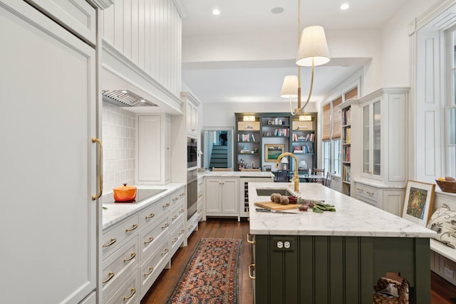 kitchen featuring pendant lighting, sink, white cabinetry, light stone countertops, and an island with sink