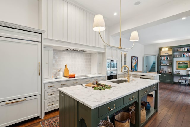 kitchen with white cabinetry, sink, hanging light fixtures, a kitchen island with sink, and light stone counters