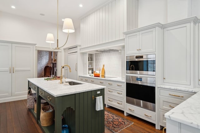 kitchen featuring decorative light fixtures, decorative backsplash, sink, a kitchen island with sink, and light stone counters