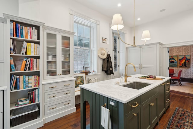 kitchen featuring dark hardwood / wood-style floors, a center island with sink, sink, hanging light fixtures, and light stone counters