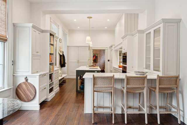 kitchen with sink, white cabinetry, hanging light fixtures, dark wood-type flooring, and a kitchen breakfast bar