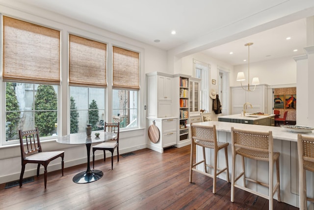 kitchen with a kitchen bar, an island with sink, dark hardwood / wood-style flooring, hanging light fixtures, and white cabinets