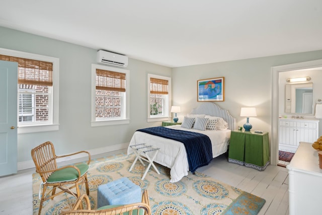 bedroom with an AC wall unit, multiple windows, and ensuite bathroom