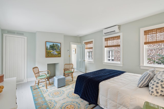 bedroom featuring an AC wall unit, multiple windows, and light hardwood / wood-style floors