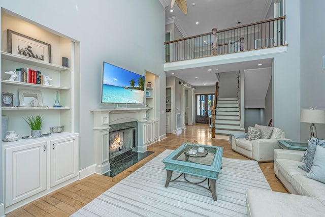 living room with light hardwood / wood-style floors, a high ceiling, built in features, and a fireplace