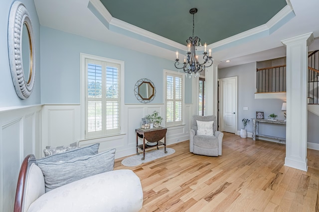 sitting room with an inviting chandelier, ornate columns, light wood-type flooring, and a raised ceiling